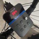 Černý ovládací modul elektronických bicích s digitálním displejem, na kterém svítí červená čísla 004. Na horní části je bílý nápis Millenium a nad ní…