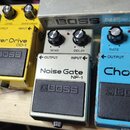Pět efektových pedálů značky BOSS v řadě. Zleva doprava jsou modrý Compression Sustainer CS-1, žlutý Over Drive OD-1, stříbrný Noise Gate NF-1, světl…