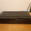 Černý výkonový zesilovač v rackovém provedení s kovovým šasi a ventilačními otvory na horní straně. Na předním panelu je bílý nápis STEREO POWER AMPL…
