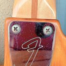 Detail zadní části krku kytary z dřeva s kovým krytem. Na chromovaném krytu je vyryto logo Fender a nápis FENDER MICRO-NECK ADJUST PAT. 3550496. Povr…