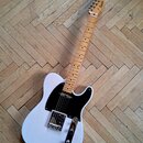 Bílá elektrická kytara typu Telecaster s černým pickguardem a hnedým javorovým hmatníkem. Na hlavě krku je viditelné logo "Squier". Nástroj vykazuje…