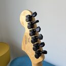 Zadní strana hlavy elektrické kytary z přírodního dřeva s šesti černými ladicími mechanismy. Na dřevě je vyryto logo Fender, text Crafted in Indonesi…