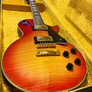 Elektrická kytara typu Les Paul s červeno-žlutým sunburst povrchem a viditnou strukturou dřeva. Nástroj má dva humbuckery, zlatý hardware a čtyři čer…