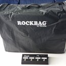 Na fotografii je černý textilní kryt s bílým nápisem ROCKBAG by Warwick. Před krytem leží černý kytarový spínací pedál značky Marshall s označením JC…