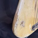 Detail korpusu elektrické basy v krémové barvě. Povrch laku vykazuje výrazné opotřebení, četné praskliny (krakelure) a rozsáhlé odřeniny, přes které…
