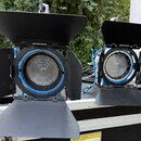 Dvě černé studiové lampy s modrými vnitřními kroužky a klapkami pro směrování světla. Svítidla jsou umístěna v černém transportním kufru s hliníkovým…