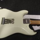 Zadní strana elektrické kytary v krémové barvě s bílým popruhem. Na kovovém krytu u krku je viditelné logo "Squier". V prostoru kobylky jsou vidět pr…