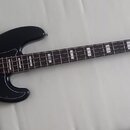 Černá elektrická basová kytara s černým pickguardem a hnědým hmatníkem. Na hlavě nástroje je bílé logo Fender a nápis DELUXE BASS SERIES. Nástroj vyk…