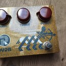 Kytarový efekt pedál v kovovém zlatavém provedení s třemi červenými ovládacími knoflíky. Nad knoflíky jsou nápisy GAIN, TREBLE a OUTPUT. V levé dolní…