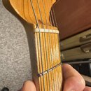 Detail krku a hlavy basové kytary z přírodního dřeva. Na hlavě je viditelna část kurzivního nápisu, ze kterého je čitelný fragment "Fende". Hmatník m…