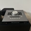 Stříbrné audio zařízení s velkým centrálním ovládacím knoflíkem a řadou bílých tlačítek. Na přední hraně je nápis UNIVERSAL AUDIO doprovázený logem.…