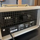 Zadní strana kytarového komba v krémovém provedení s černou mřížkou a kovovými rohy. Na černém štítku jsou nápisy POWER SOURCE: 230V~50Hz, POWER CONS…
