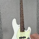 Bílá elektrická basová kytara s hnědým hmatníkem a světlým dřevěným hlavním koncem. Na hlavě je viditelné logo Squier. Tělo nástroje vykazuje výrazné…