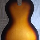 Zadní strana kytary s žlutě-hnědým přechodovým lakem (sunburst). V horní části těla je kovový spojovacídeska s nápisem "MADE IN KOREA". Povrch laku v…