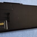 Zadní strana černé elektrické kytary s lesklým povrchem. V dolní části je viditelný štítek s nápisy BATTERY COMPARTMENT, connect battery before opera…