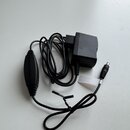 Černý sustain pedál s připojeným napájecím adaptérem. Na bílém papírovém pásku kolem kabelu je viditelný nápis ROTRA 22. Povrch pedálu i adaptéru je…