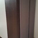 Fotografie zobrazuje vysoký, úzký reproduktor s tmavě hnědým povrchem imitujícím dřevo. Přední strana je zakrytá dvěma ségmi šedé textilní maskovací…