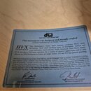 Fotografie detailu štítku přilepeného k dřevěnému povrchu. Štítek obsahuje logo dw drums, nápis Performance series™ a text „This instrument was desig…