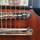 Detailní pohled na most a kobylku elektrické kytary s hnědým dřevěným povrchem. Nástroj má chromované kovové komponenty a černý pickguard. Na černém…