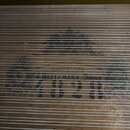 Detail dřevěného povrchu nástroje s dekorativním nápisem a ornamenty. Je zde vidět text „MEDAILLEN IN SAMMLICHEN AUSSTELLUNGEN“ a pod ním výrazný náp…