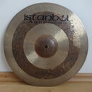 Kovový činel zlatavé barvy s viditelným Oxidováním a tmavými skvrnami v prostřední části. V horní části je černý nápis istanbul Agop Handmade cymbals…