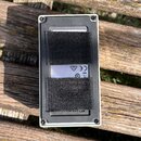 Fotografie zachycuje zadní stranu efekt pedálu v bílém rámu s černým plastovým panelem. Na panelu jsou přilepené dva kusy černého suchého zipu, pod k…