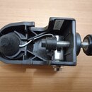 Černý plastový držák s kovovým šroubem a knurlovaným knoflíkem. Na horní části je nalepený bílý štítek s označením 27F4074. V levé části je umístěná…