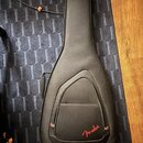 Černý polotvrdý pouzdro na kytaru s rukojetí. V dolní části je červené logo Fender. Povrch materiálu vykazuje mírné opotřebení a zaprášení.