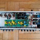 Fotografie zachycuje vnitřek elektronického zařízení v kovovém šasi. Uvnitř jsou vidět zapojené desky plošných spojů, kondenzátory, rezistory a kabel…