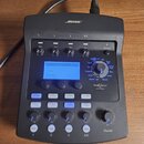 Černý mixovací pult značky BOSE. Zařízení obsahuje displej s nápisy CH 1, Reverb, Mix a Bypass, čtyři Trim knofíky, čtyři tlačítka CH Edit, čtyři tla…