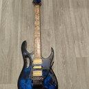Elektrická kytara s modře a černě strakatým povrchem korpusu a hnědým hmatníkem s modrými ornamenty listů. Na hlavě je bílý nápis Ibanez. Nástroj má…