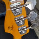 Záběr na hlavu basové kytary v žlutohnědé barvě s čtyřmi chromovanými ladičkami. Na zadní straně hlavy je černý nápis „Designed and Backed by Fender®…