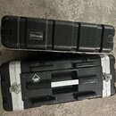 Dvě černé transportní bedny z texturovaného materiálu s hliníkovými hranami. Horní bedna má nalepený oválný štítek s nápisem ROCKCASE by Thomann. Spo…