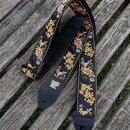 Černý popruh na hudební nástroj s žlutým květinovým vzorem. Na jednom z konců je kousek černé kůže s vyraženým logem ERNIE BALL. Druhý konec má v kůž…
