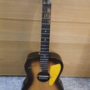 Akustická kytara s tmavým, přechodovým povrchem (sunburst). Na hlavě je bílý nápis CABALLERO a na korpusu vlevo od otvoru nápis astano. Nástroj má žl…