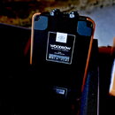 Zadní strana kompaktního černého přístroje s oranžovými okraji. Na bílém štítku je uveden nápis WOODROW, pod ním text 56 Instrument Amplifier a dále…