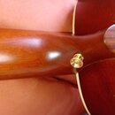 Detailní pohled na spoj hned krku a korpusu akustické kytary z dřeva s reddish-brown povrchem. V místě spoje je viditelný jeden zlatý šroub s vrškem…