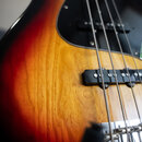 Detailní pohled na tělo elektrické basové kytary s barevným přechodem od červené přes žlutou k černé. Nástroj má černý pickguard a dva snímače s čern…