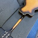 Zadní strana akustické kytary s barevným přechodem od žluté středu k tmavě hnědým okrajům. Nástroj má dřevěné tělo, hnedý krk a tmavě hnědou hlavu s…