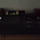 Sada audio vybavení tvořící centrum s míchací deskou, dvěma dřevěnými reproduktory a rackovým zařízením. Na černém zařízení v horní části je červené…