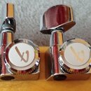 Detail hlavy nástroje s šesti chromovanými ladicími mechanismy. Na bílých krytkách knoflíků je u všech mechanismů umístěno červenobílé logo ve tvaru…