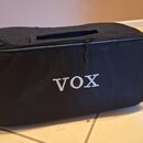 Černý polstrovaný obal z textilie s zipem a madlem v horní části. Na přední straně je bílý nápis VOX. Povrch obalu vypadá čistě a bez viditelného opo…