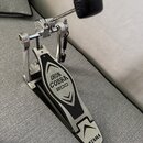 Stříbrný kovový pedál na basový buben s černým stupňem. Na stupni je nápis IRON COBRA 200 a v dolní části logo TAMA. Nástroj vykazuje mírné známky po…