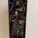 Fotografie zachycuje vnitřek černého plastového šasi efekt pedálu. Uvnitř je umístěna elektronická deska s nápisem Theolina WAH a označením PW v2. Na…