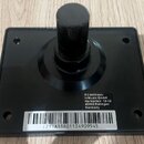 Černý plastový pedál nebo spínač s kulatým knoflíkem uprostřed. Na spodní části je bílá nálepka s textem „EU Address: inMusic GmbH Harkortstr. 12-32…