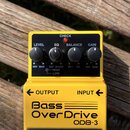 Žlutý efekt pedál s nápisy Bass OverDrive a ODB-3. Horní panel obsahuje čtyři černé ovládací knoflíky s popisky LEVEL, EQ, BALANCE a GAIN, červenou k…