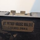 Detail kovového štítku připevněného na černý, opotřebovaný povrch pouzdra. Na štítku je doslovný nápis ANT. PETROF-HRADEC KRÁLOVÉ CZECHOSLOVAKIA. Pov…