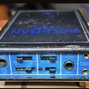 Černý efektový procesor s modrým předním panelem. Na horní části je modrý nápis ROCKMAN X100. Přední panel obsahuje dva posuvníky s popisky NORM a VO…
