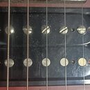 Fotografie zachycuje dva černý humbuckery s plastovými krytkami na červeném povrchu kytary. Horní snímač má v polosách viditelné šrouby, spodní sníma…