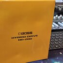 Žlutá papírová krabice s nápisy BOSS, HYBRID DRIVE a OD-200. Povrch krabice vykazuje mírné pomačkání v horní části a drobné záhyby. V pozadí je vidět…